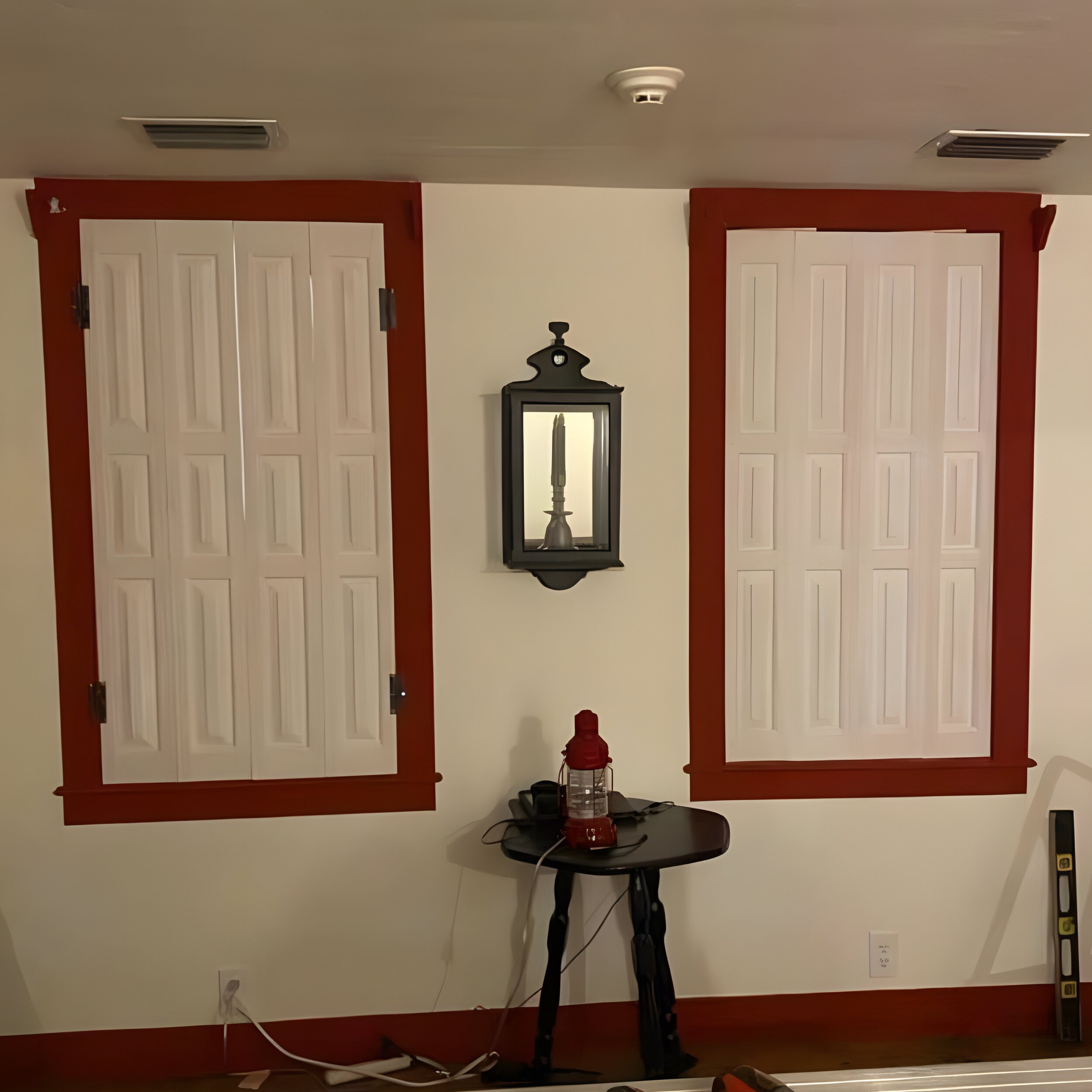 Two white raised-panel shutters installed in bold red window trim with wall lantern